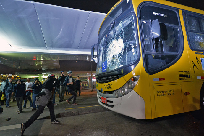 A masked demonstrator throws a stone against a bus after a demonstration against rising public transport costs and demanding better public services in Sao Paulo, Brazil, on October 25, 2013. (AFP Photo/Nelson Almeida)