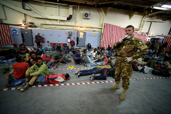 Some of the 219 migrants sit inside the Italian Navy amphibious assault ship San Marco after being rescued off the island of Lampedusa on October 25, 2013. (AFP Photo / Filippo Monteforte)