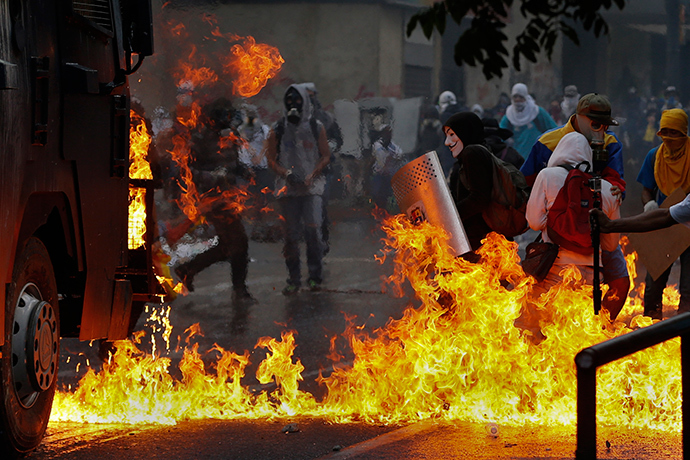 Um manifestante anti-governo, usando uma máscara de Guy Fawkes, está com um escudo perto de chamas de coquetéis molotov jogados em um canhão de água por manifestantes anti-governamentais durante os distúrbios em Caracas 20 abr 2014 (Reuters / Jorge Silva)