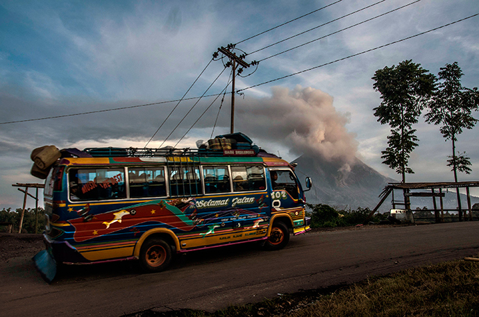 A public bus drives past Mount Sinabung volcano (background) as it spews volcanic ashes into the air in Karo district in North Sumatra province on June 10, 2015 (AFP Photo / Sutanta Aditya)